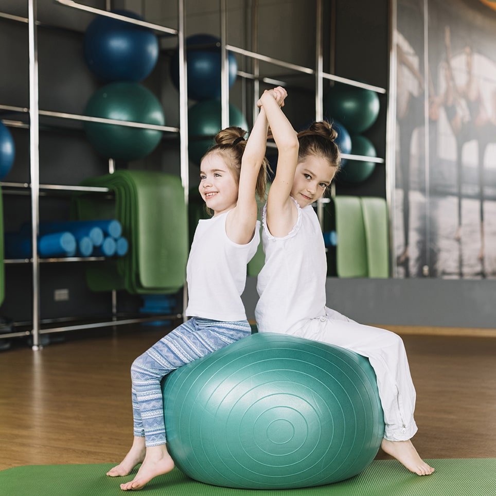 two-little-girl-sitting-back-back-exercising-ball-together-min